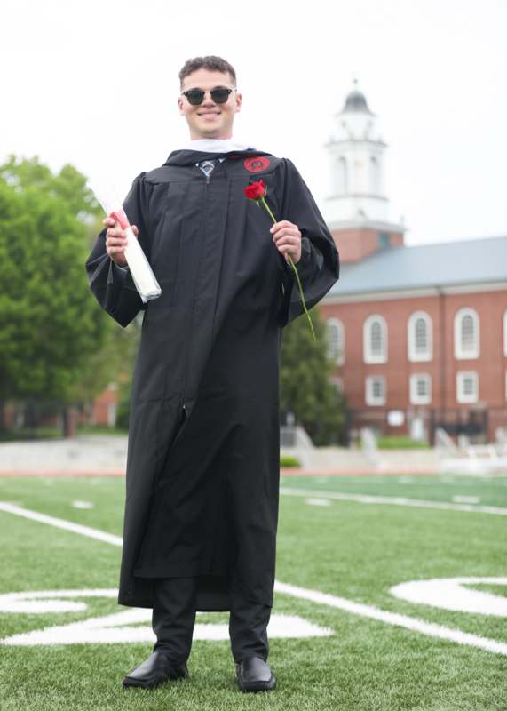 a man in a graduation gown holding a rose and a diploma