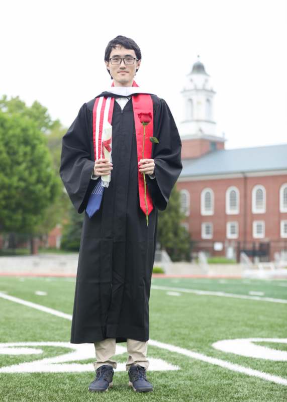 a man in a graduation gown holding a rose