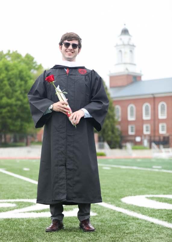 a man in a graduation gown holding a rose