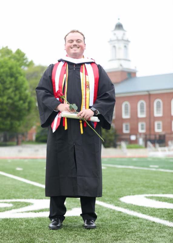 a man in a graduation gown holding a rose