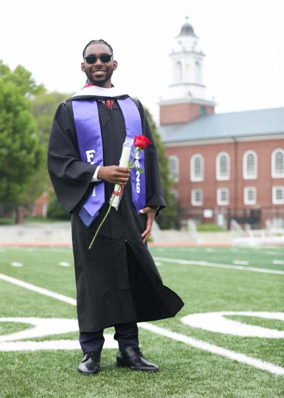 a man in a graduation gown holding a rose
