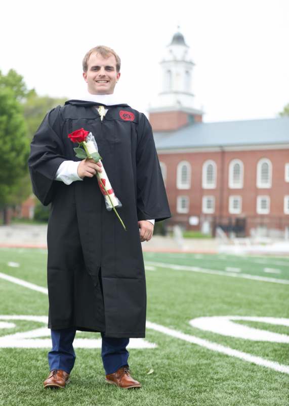 a man in a graduation gown holding a rose