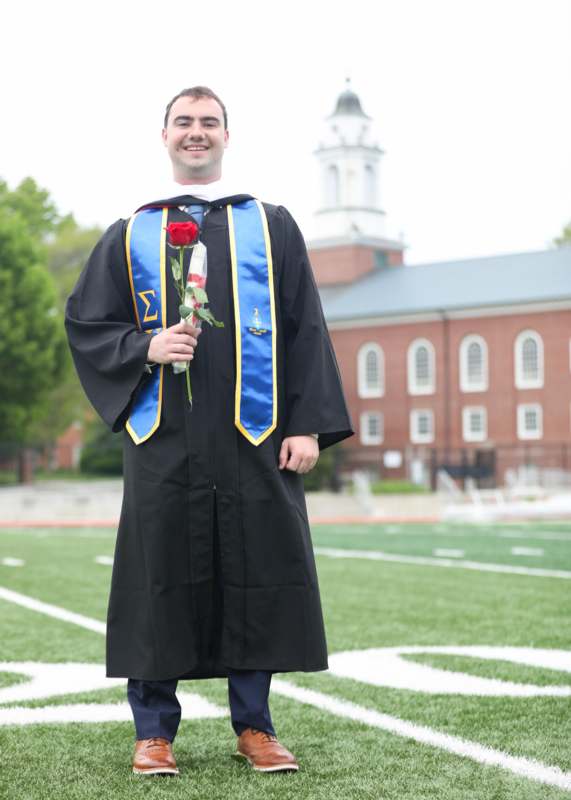 a man in a graduation gown holding a rose