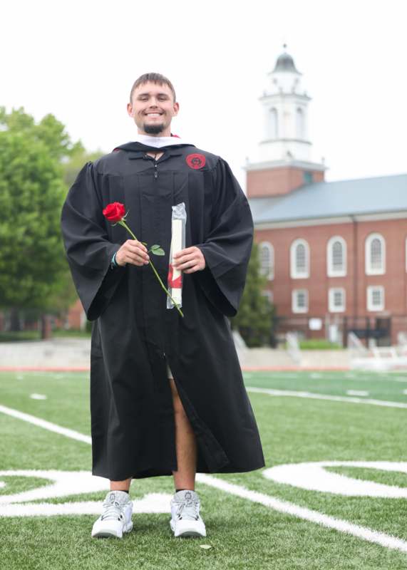 a man in a graduation gown holding a rose