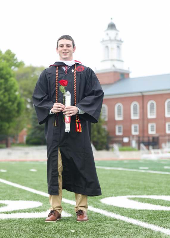 a man in a graduation gown holding a rose and a bottle