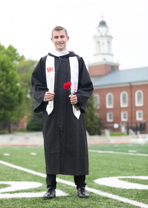 a man in a graduation gown holding a rose and a diploma