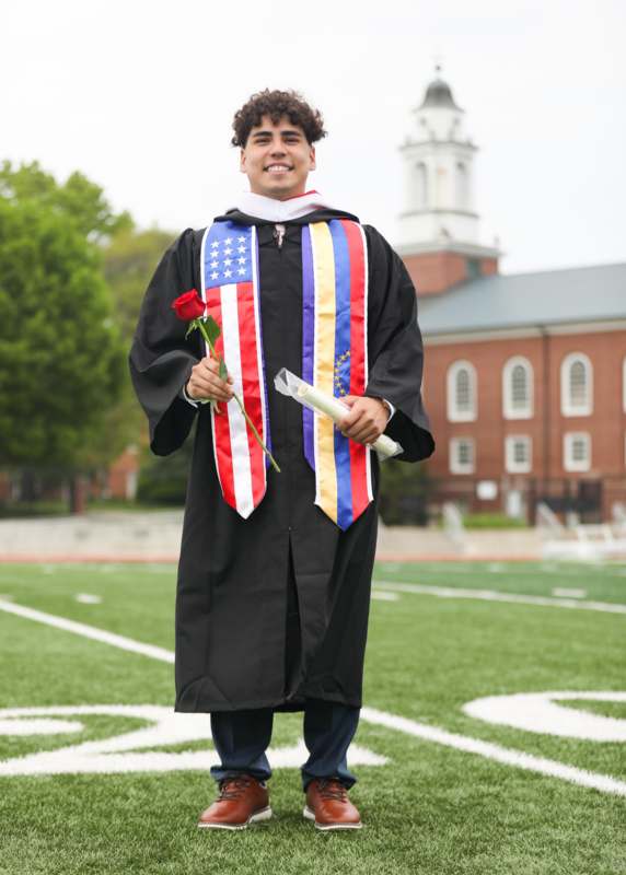 a man in a graduation gown holding a rose and a diploma