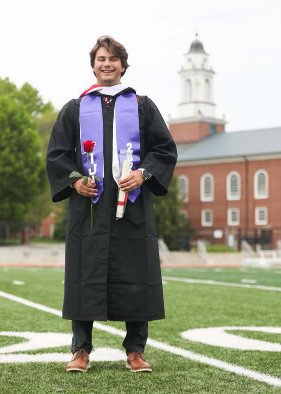 a man in a graduation gown holding a rose and a diploma