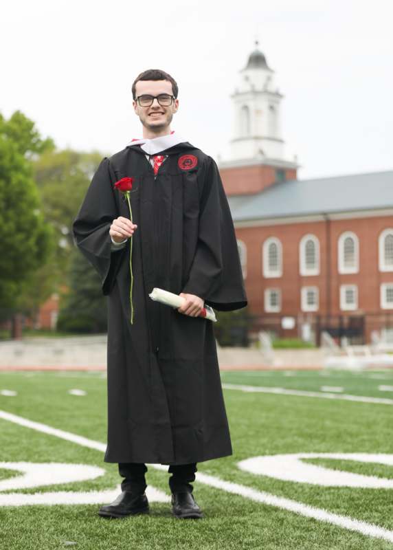a man in a graduation gown holding a rose