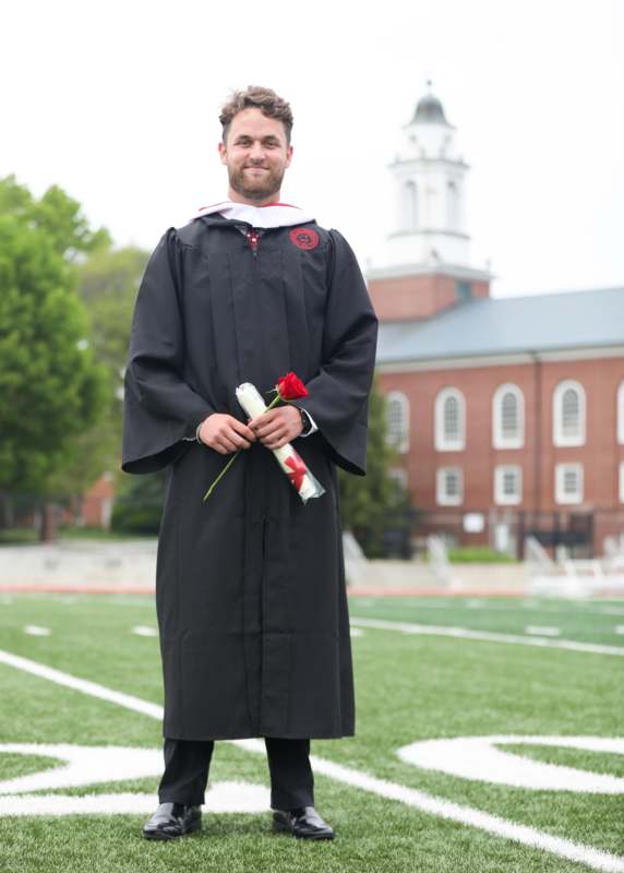 a man in a graduation gown holding a rose