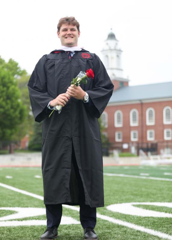 a man in a graduation gown holding a rose
