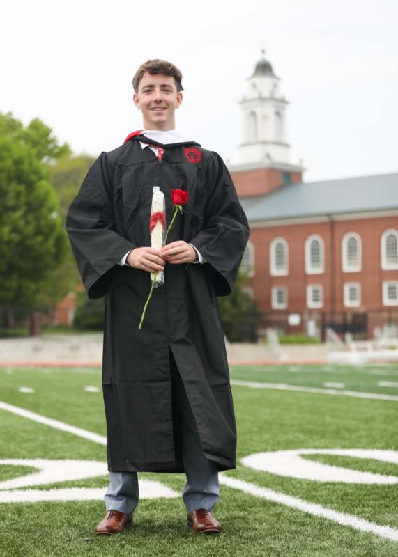 a man in a graduation gown holding a rose