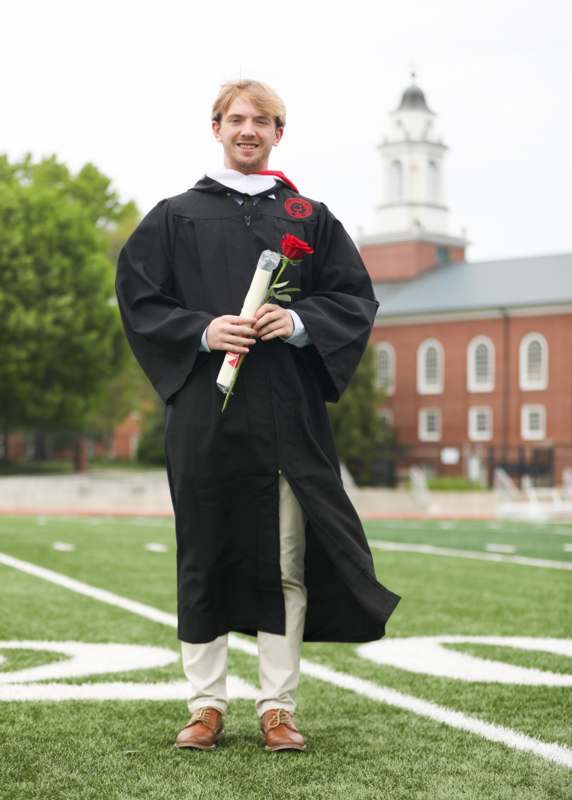 a man in a graduation gown holding a rose and a diploma