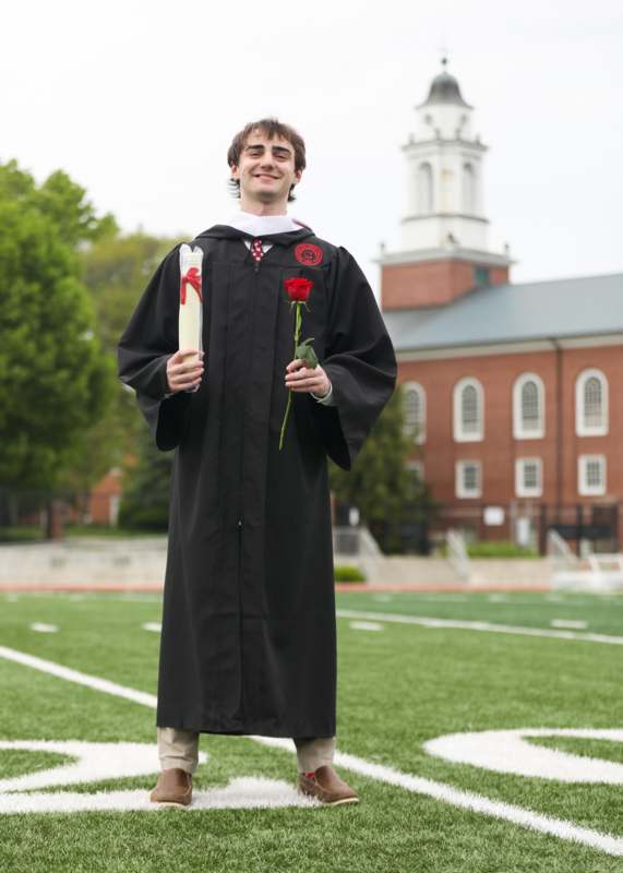 a man in a graduation gown holding a rose and a diploma