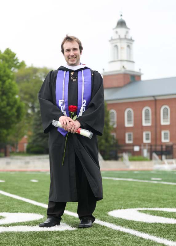 a man in a graduation gown holding a rose