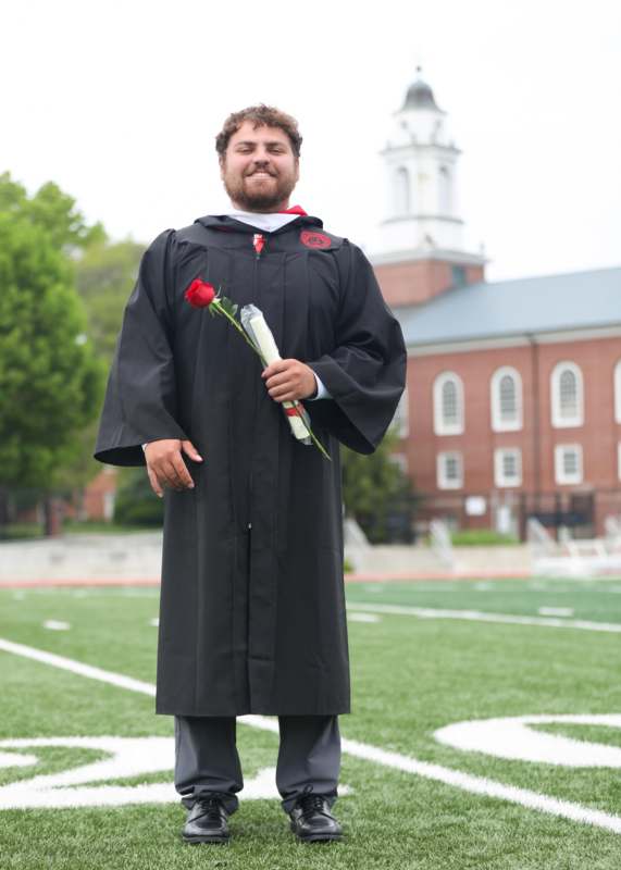 a man in a graduation gown holding a rose