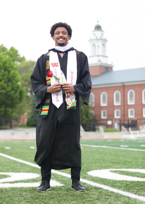a man in a graduation gown holding a rose and standing on a football field