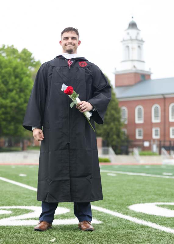 a man in a graduation gown holding a rose