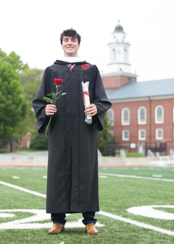 a man in a graduation gown holding a rose and diploma