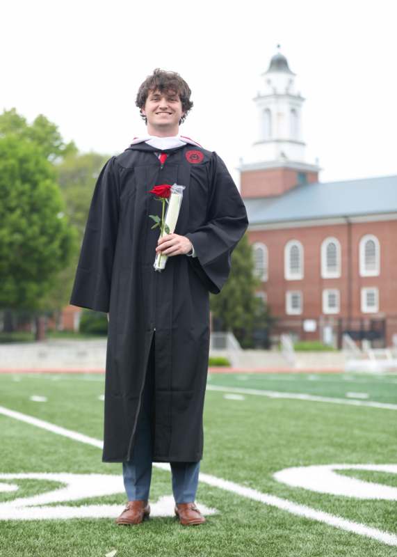 a man in a graduation gown holding a rose