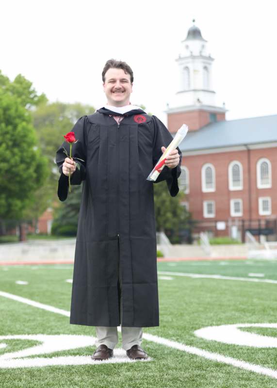 a man in a graduation gown holding a rose and a diploma