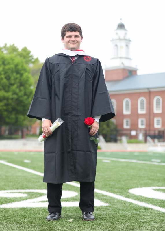 a man in a graduation gown holding a rose and a diploma