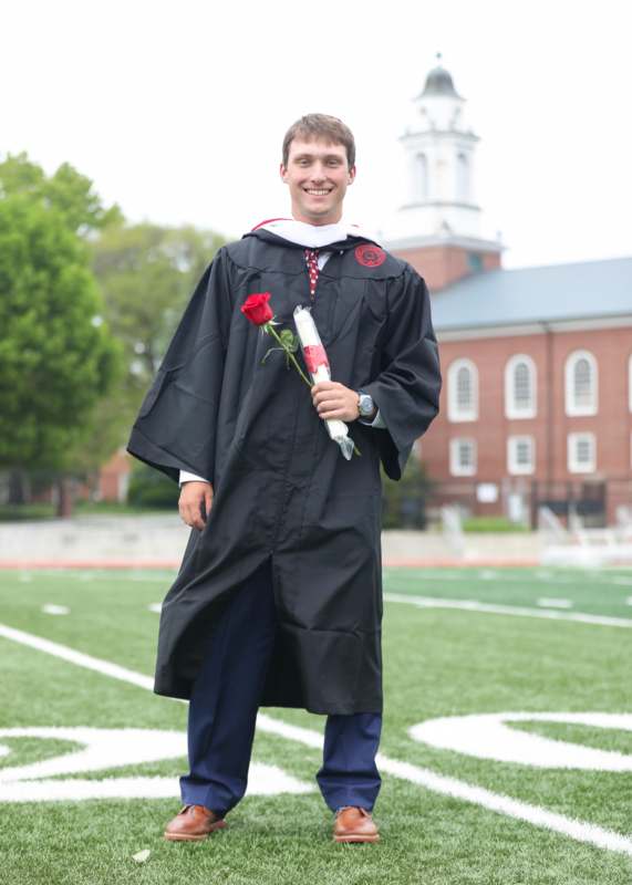 a man in a graduation gown holding a rose