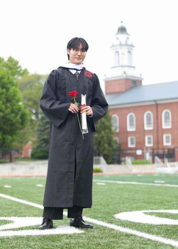 a man in a graduation gown holding a rose and a diploma