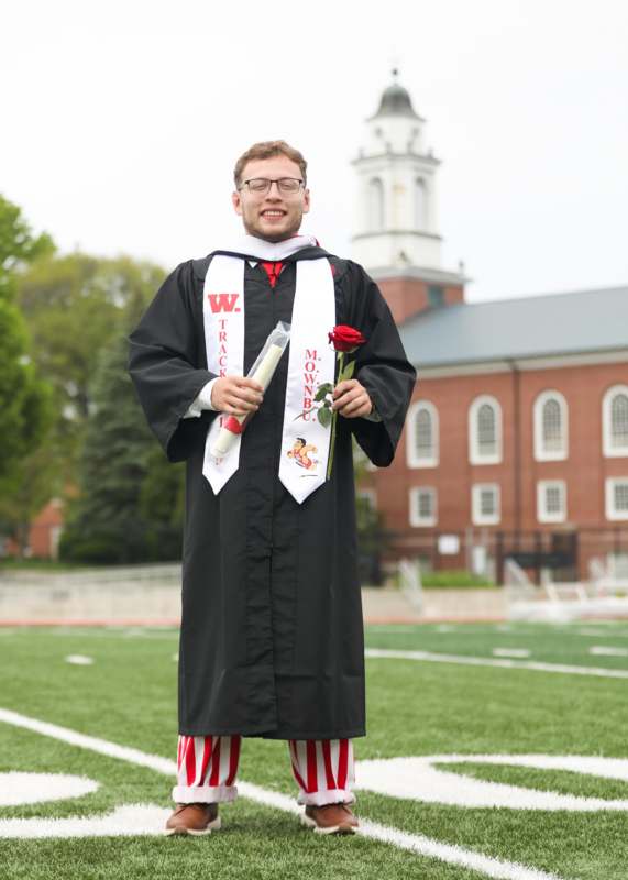 a man in a graduation gown holding a rose and a diploma