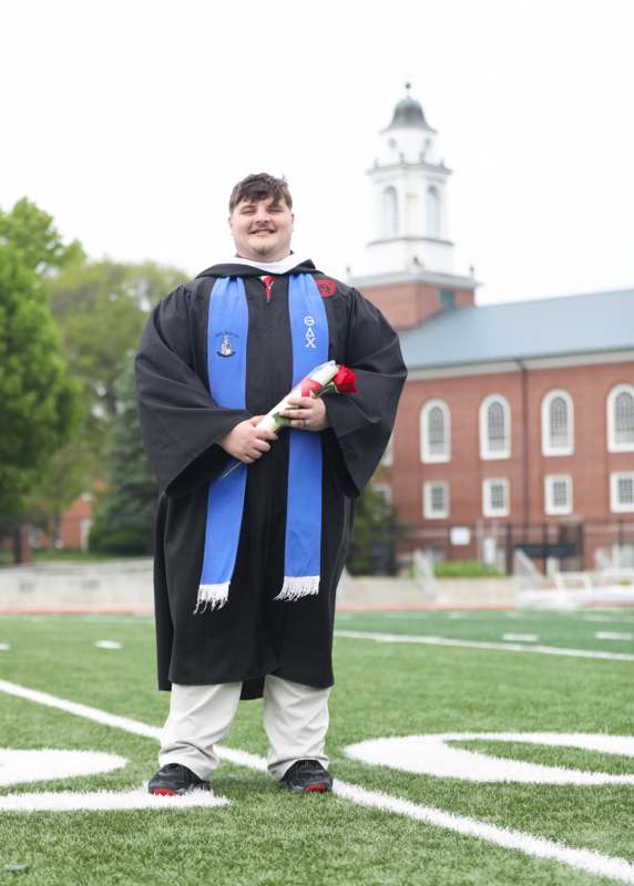 a man in a graduation gown holding a rose and a diploma