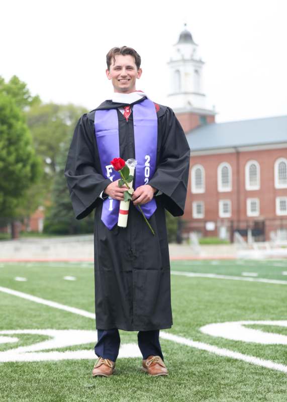 a man in a graduation gown holding a rose and a diploma