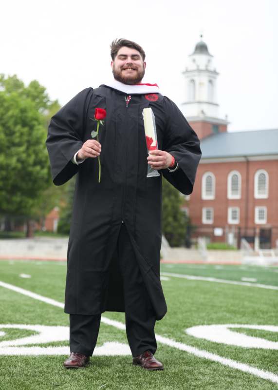 a man in a graduation gown holding a rose and a diploma