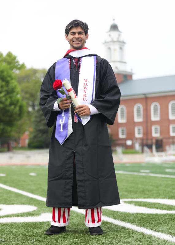 a man in a graduation gown holding a rose and a diploma