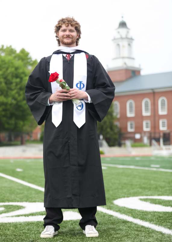 a man in a graduation gown holding a rose