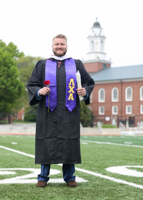a man in a graduation gown holding a rose and a diploma