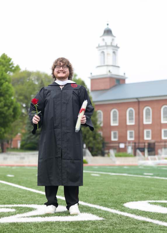 a man in a graduation gown holding a rose