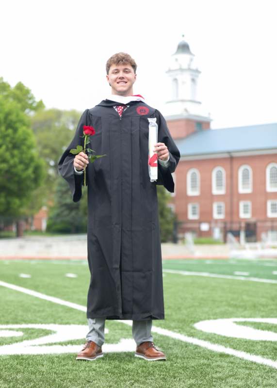 a man in a graduation gown holding a rose and diploma