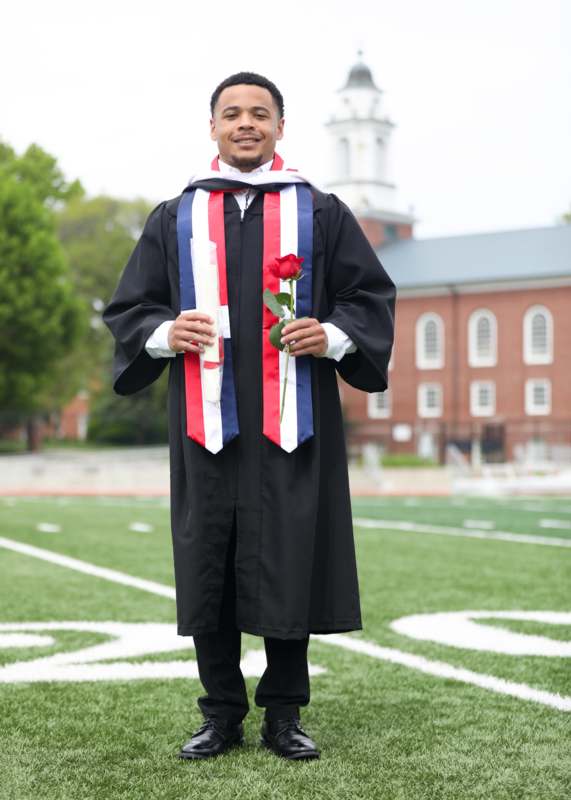 a man in a graduation gown holding a rose