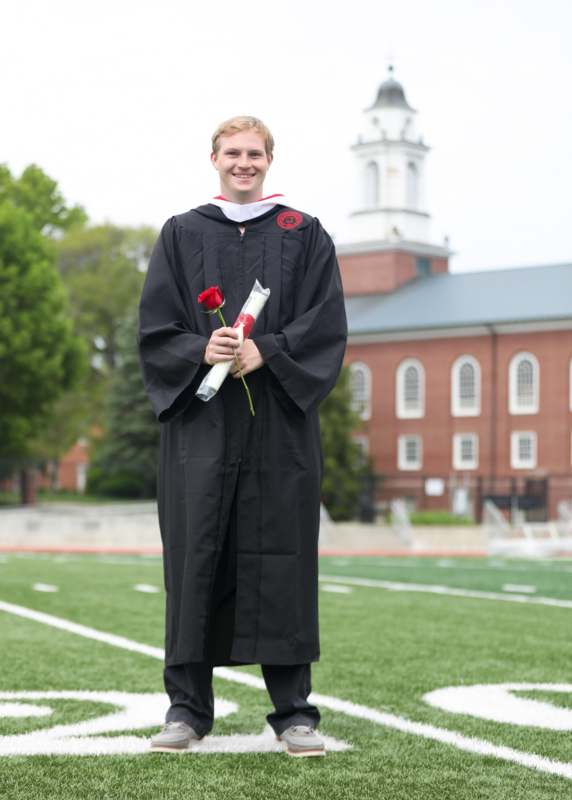 a man in a graduation gown holding a rose and a diploma