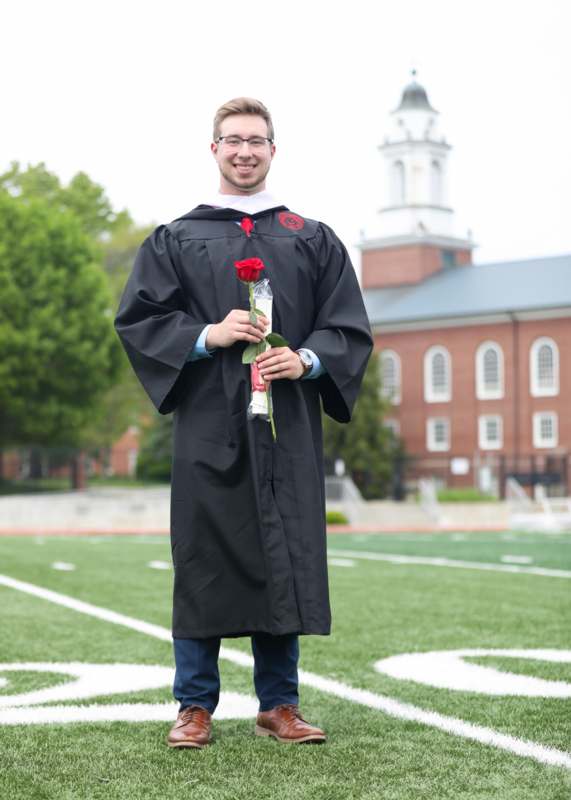 a man in a graduation gown holding a rose