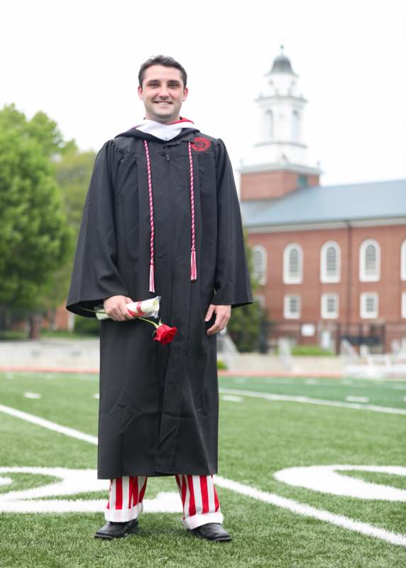 a man in a graduation gown holding a rose