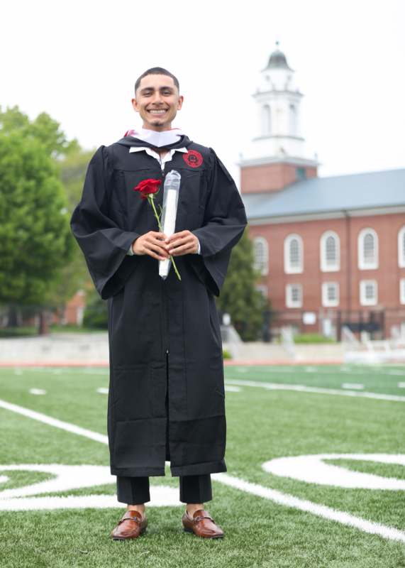 a man in a graduation gown holding a rose