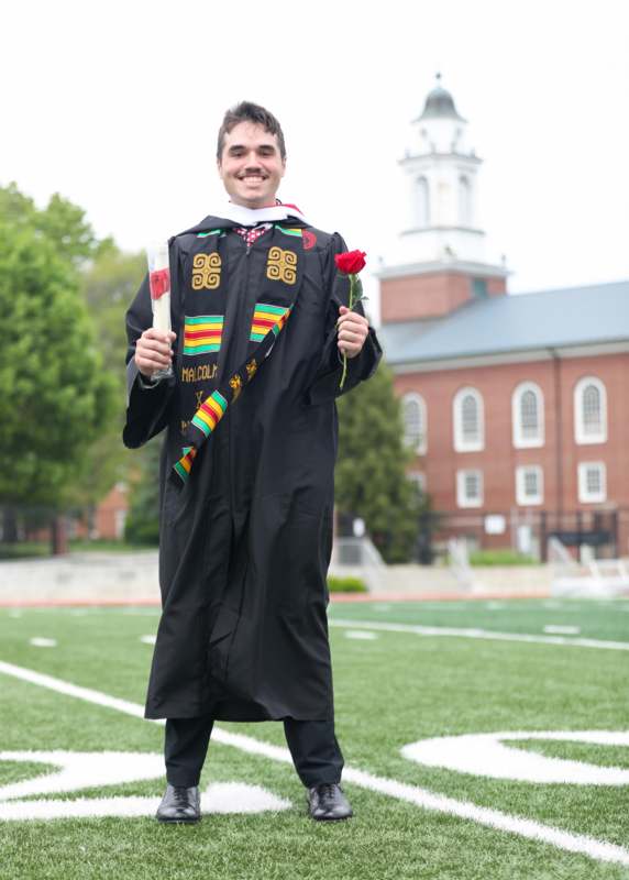 a man in a graduation gown holding a rose and a diploma