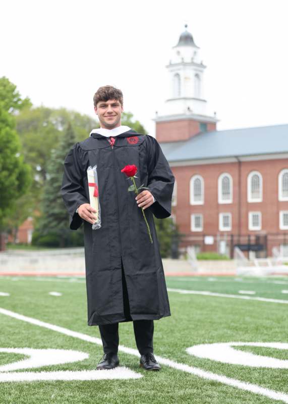 a man in a graduation gown holding a rose and a red rose