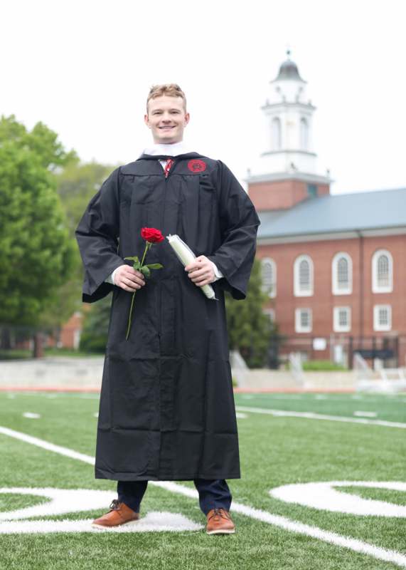 a man in a graduation gown holding a rose and a book
