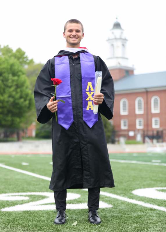 a man in a graduation gown holding a rose and a diploma
