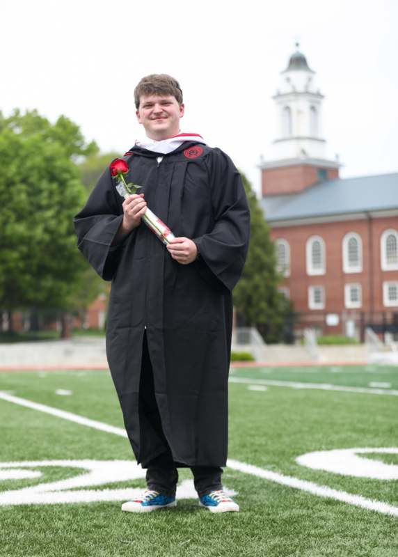 a man in a graduation gown holding a rose