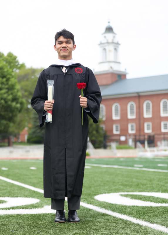 a man in a graduation gown holding a rose and a red rose