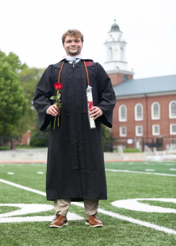a man in a graduation gown holding a rose and a diploma