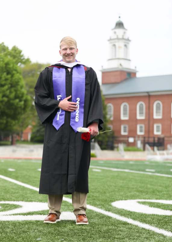 a man in a graduation gown holding a rose and a flower